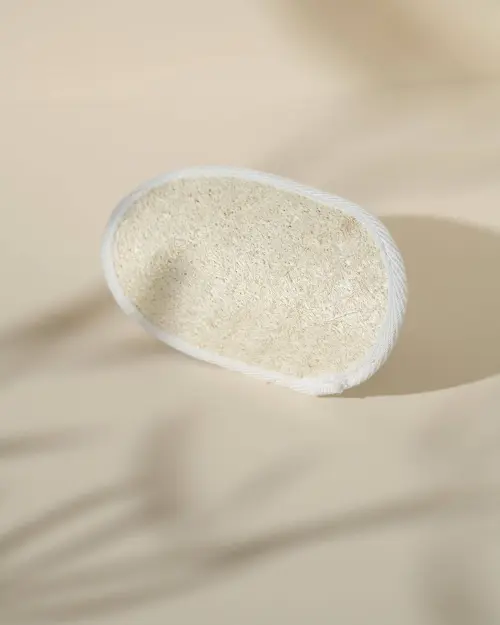 Ovalen loofa balnéo in plantaardige vezels met witte rand op beige achtergrond