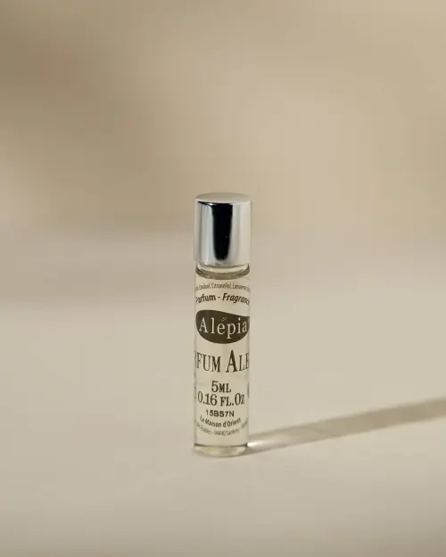 Roll-on Le parfum Alepia in zijn glazen flesje van 5 ml met zilveren dop op beige achtergrond