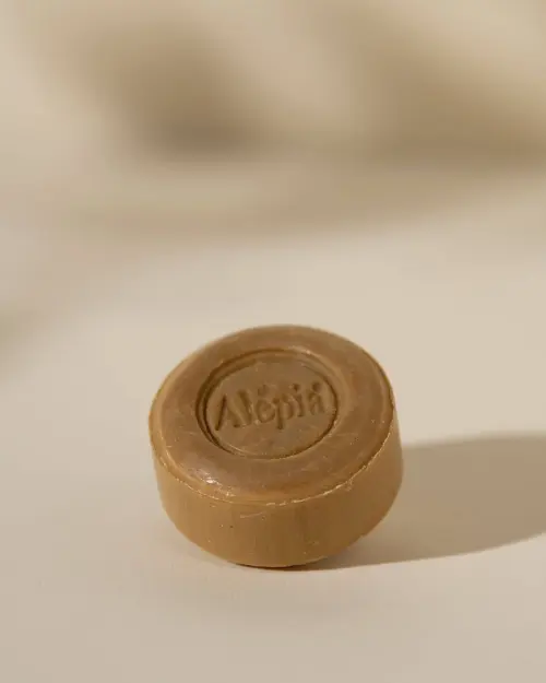 Ronde beige scheerzeep van Aleppo gegraveerd met het logo Alepia op neutrale achtergrond