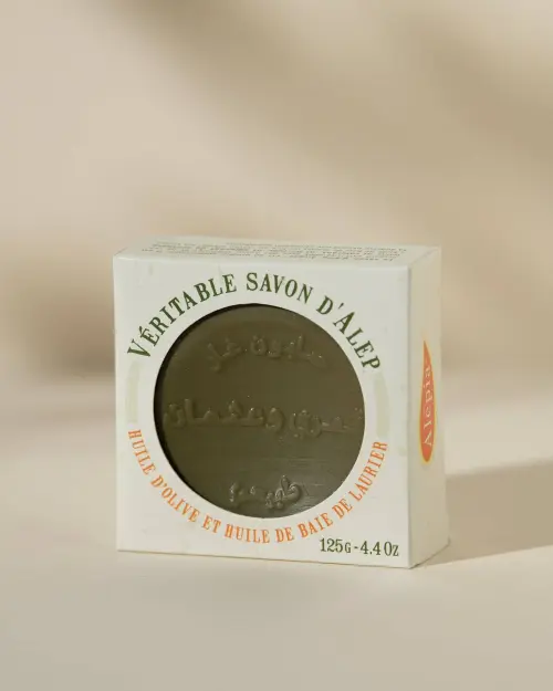 Jabón de Alepo extra-suave Alepia de 125 g, pastilla redonda verde oliva visible en su caja blanca calada