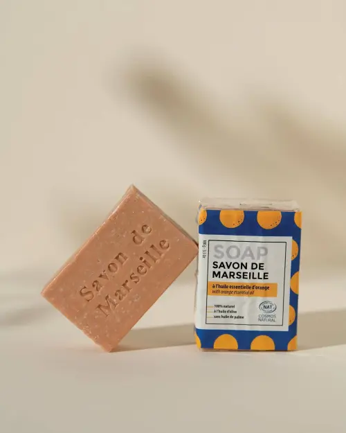 Marseillezeep met sinaasappelparfum, een gegraveerde zeep zonder verpakking naast een zeep in folie van 100 g
