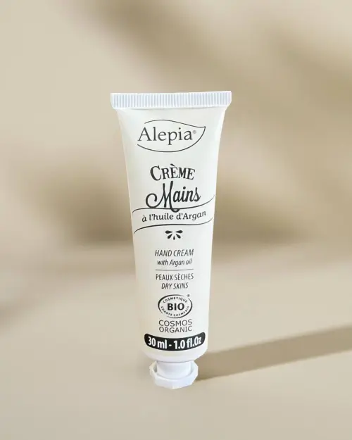 Crema de manos bio con aceite de argán Alepia en tubo blanco de 30 ml colocado de pie sobre fondo beige