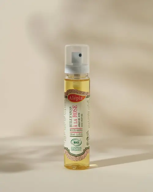 Aceite de argán ecológico con rosa Alepia en frasco spray transparente de 100 ml sobre fondo beige