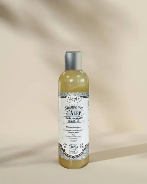 Aleppo-Shampoo Bio mit Schwarzkümmelöl Alepia in einer 250-ml-Flasche mit bernsteinfarbener Flüssigkeit auf beigem Hintergrund