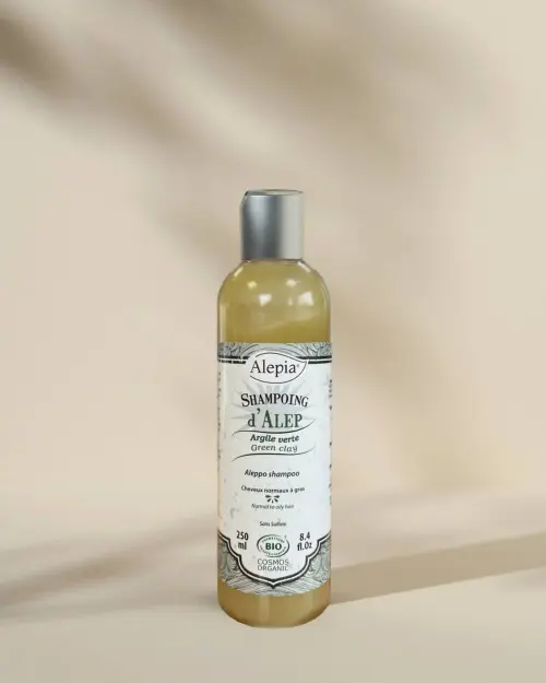 Champú de Alepo bio con arcilla verde Alepia en frasco transparente de 250 ml sobre fondo beige con sombras