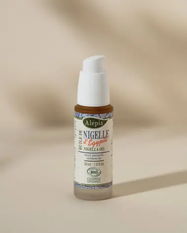 Biologische Nigella-olie van Alepia in een pompflacon van matglas van 30 ml op een beige achtergrond