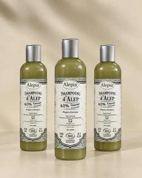 Tres frascos de champú de Alepo bio 40% laurel Alepia de 250 ml alineados sobre fondo beige