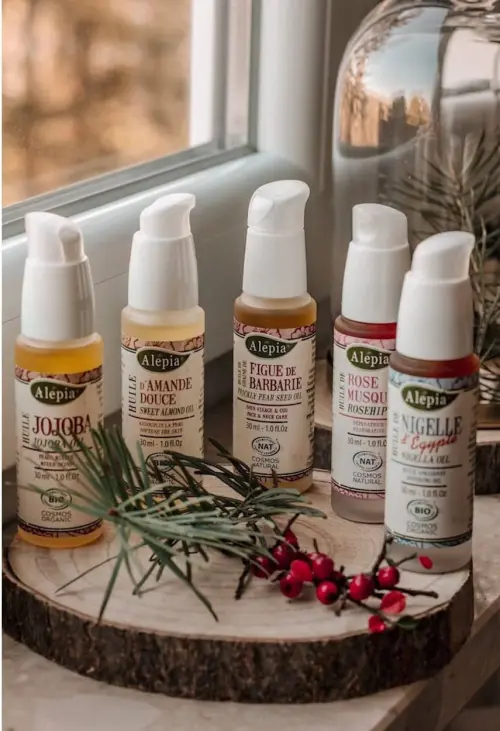 La Preciosa Colección Alepia, cinco frascos de aceites vegetales con dosificador colocados sobre un tronco de madera decorado